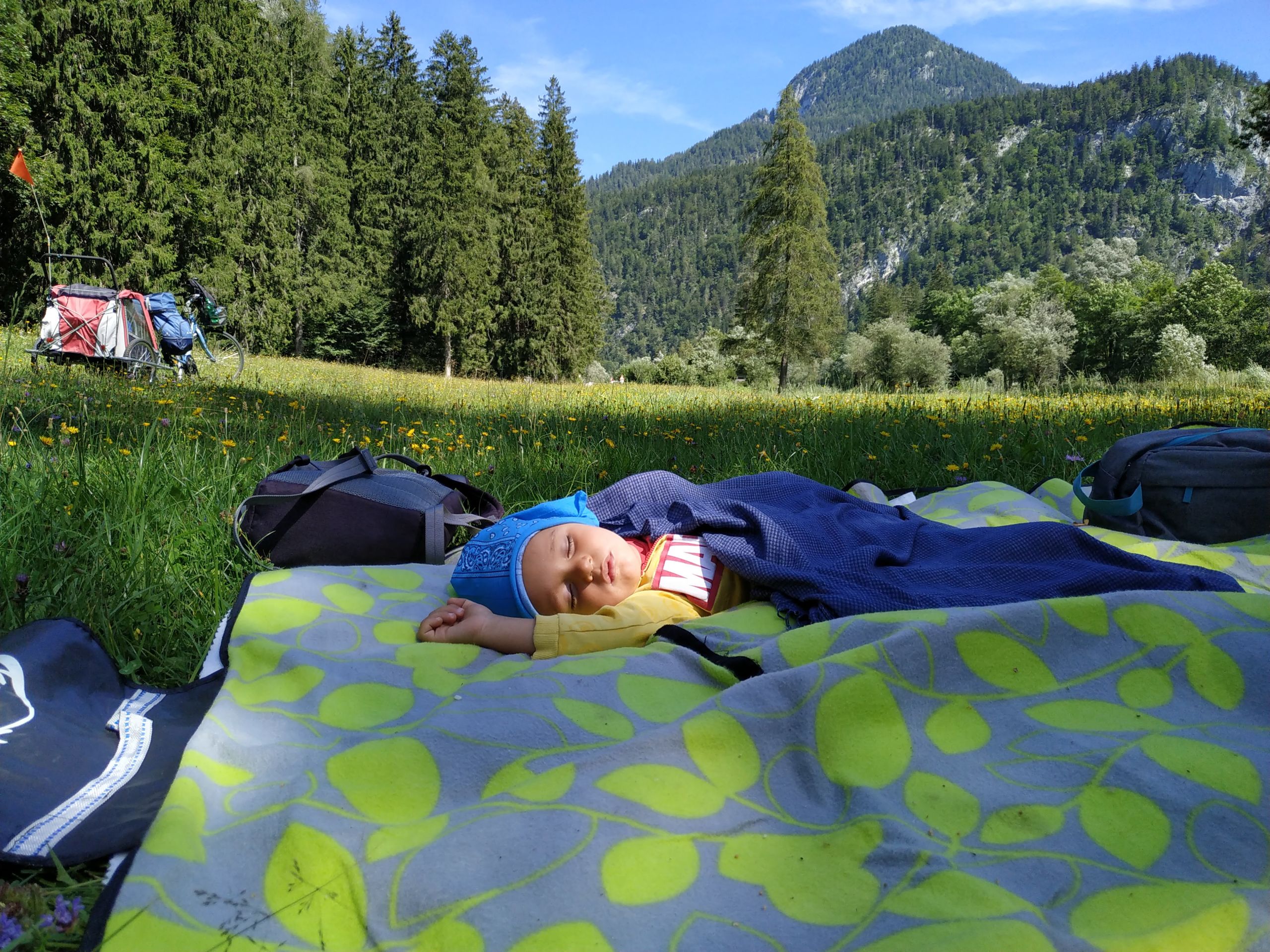Bambino che dorme su un telo da campeggio in mezzo alla natura alpina.